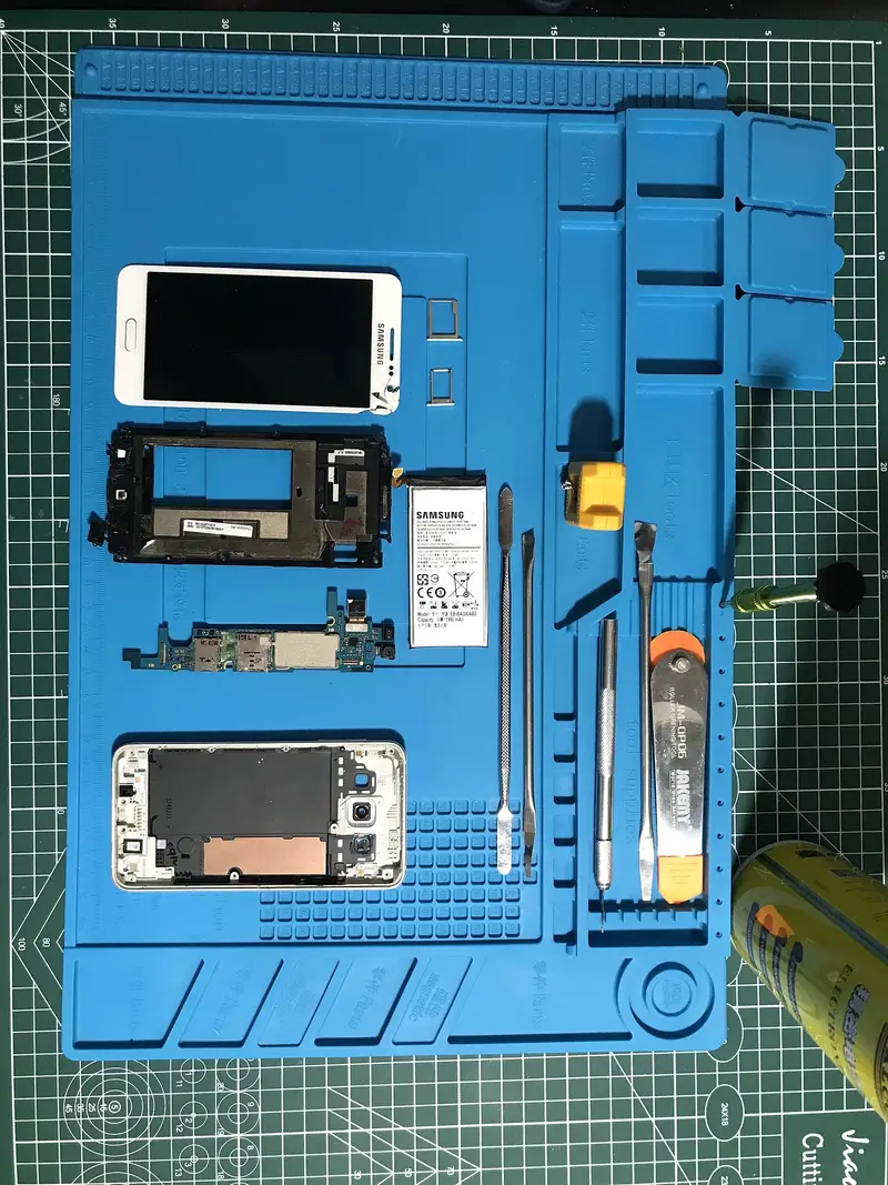 Tamir matında dizilmiş, parçalarına ayrılmış Samsung Galaxy telefon: ekran, kasa, anakart ve batarya