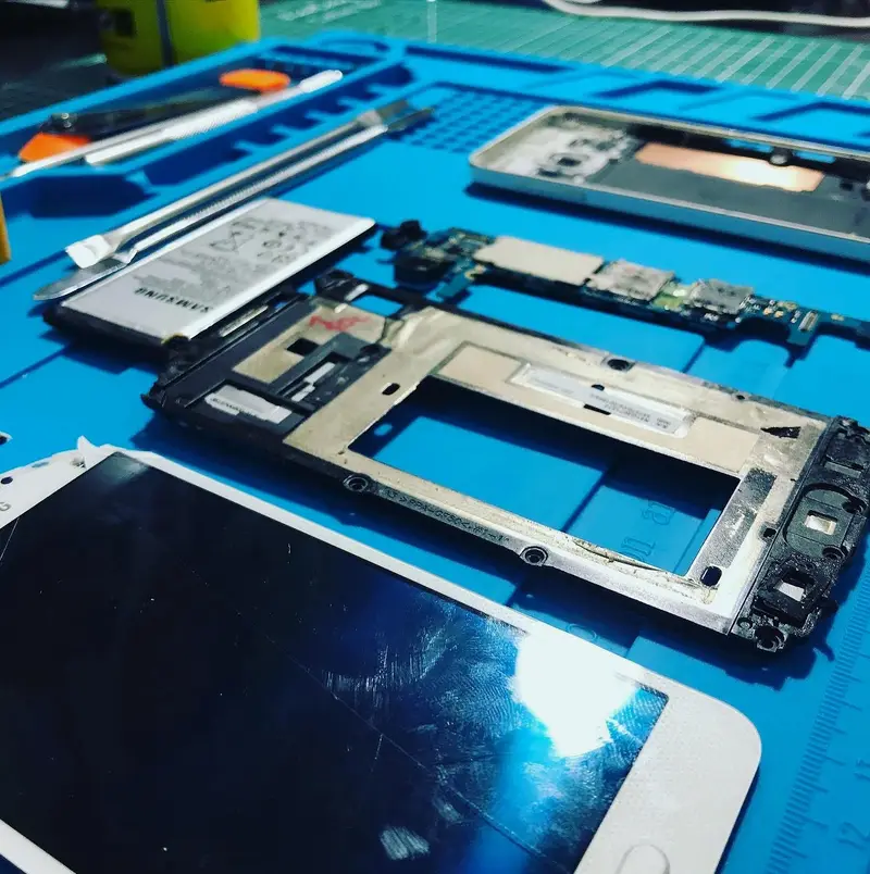 Mavi silikon tamir matında sökülmüş Samsung telefonun ekranı, çerçevesi, anakartı ve bataryası